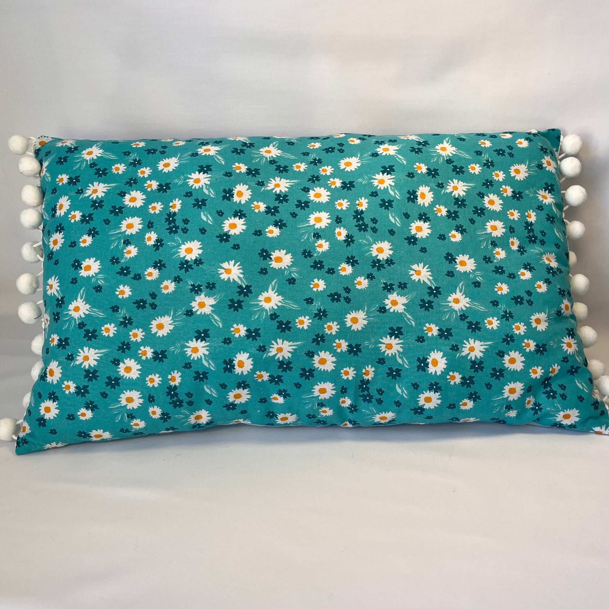 Teal rectangular pillow with white and yellow daisy pattern and white pom-pom trim