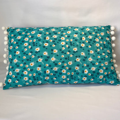 Teal rectangular pillow with white and yellow daisy pattern and white pom-pom trim