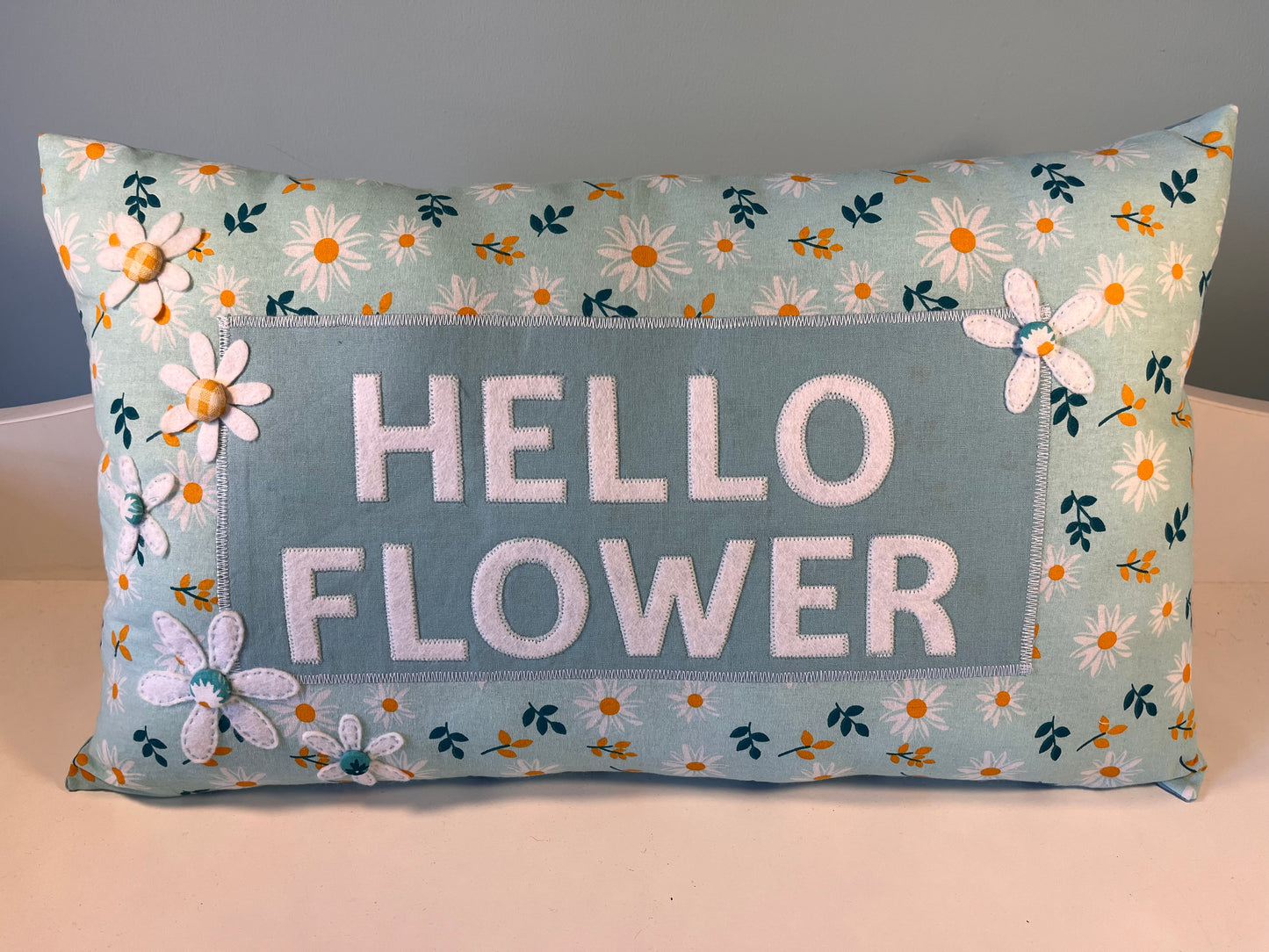 Light blue pillow with daisy print and embroidered text Hello Flower