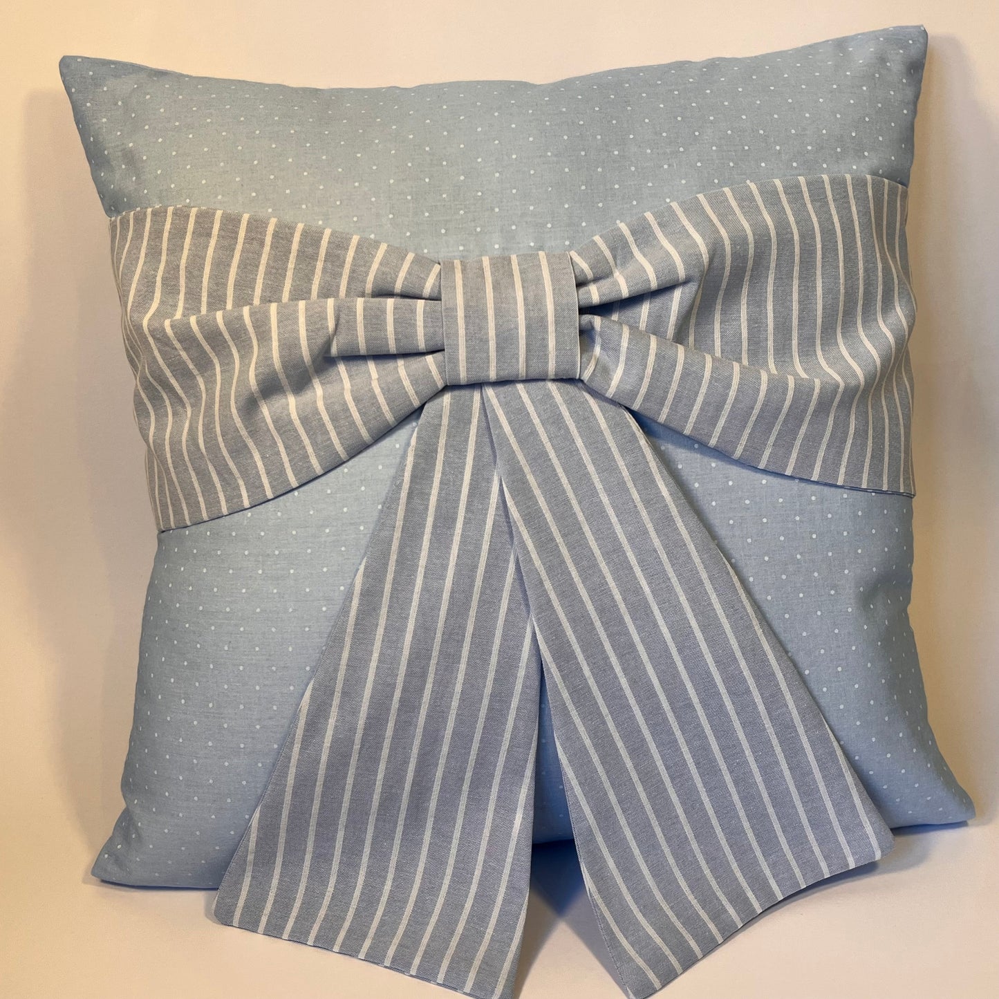 Light blue pillow with white polka dots and a large striped bow in the center