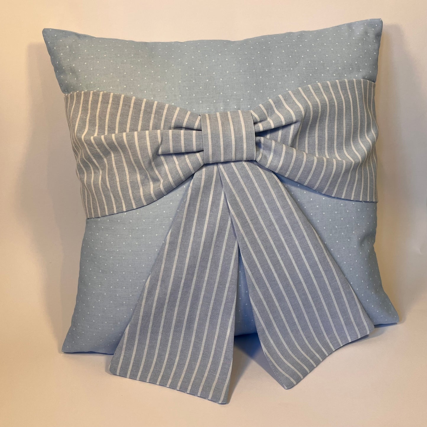 Light blue polka dot pillow with a large striped bow in the center