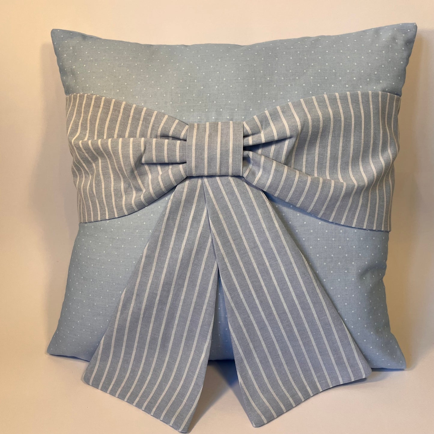 Light blue pillow with white polka dots and a large striped bow in the center