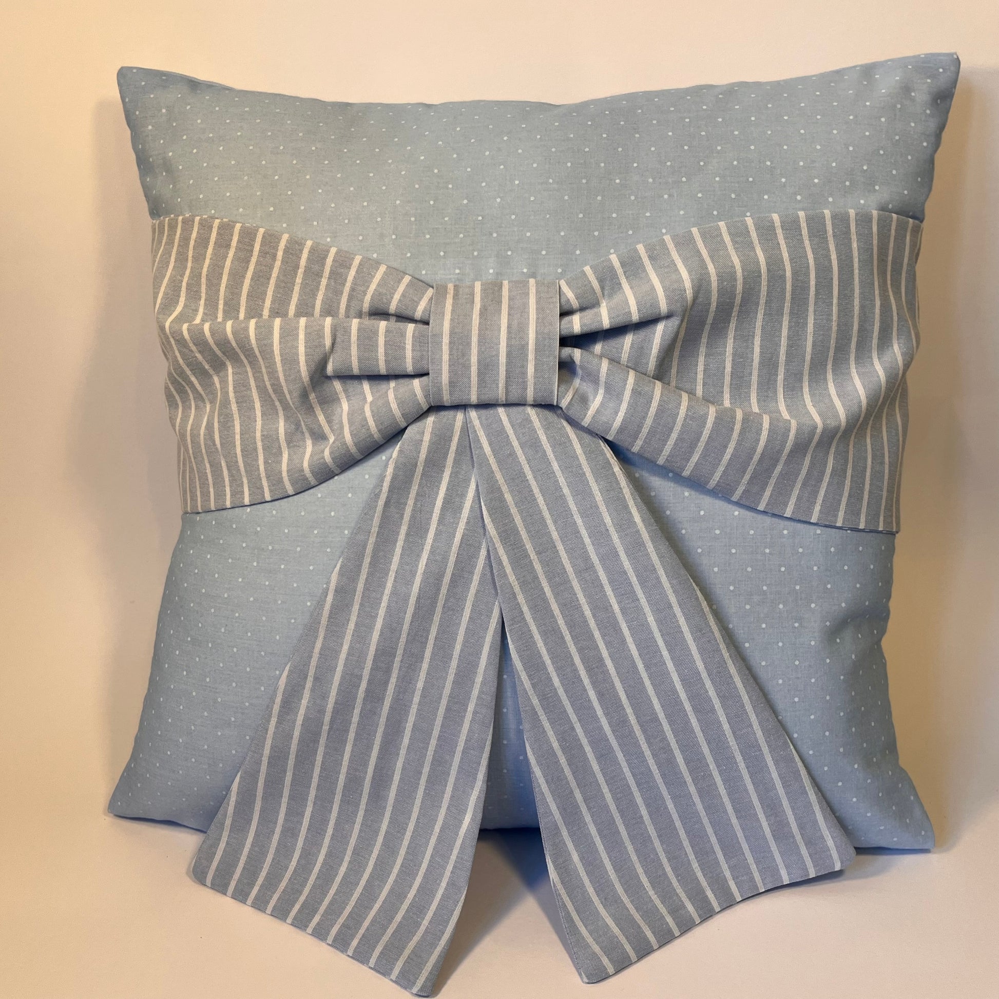Light blue pillow with white polka dots and a large striped bow in the center
