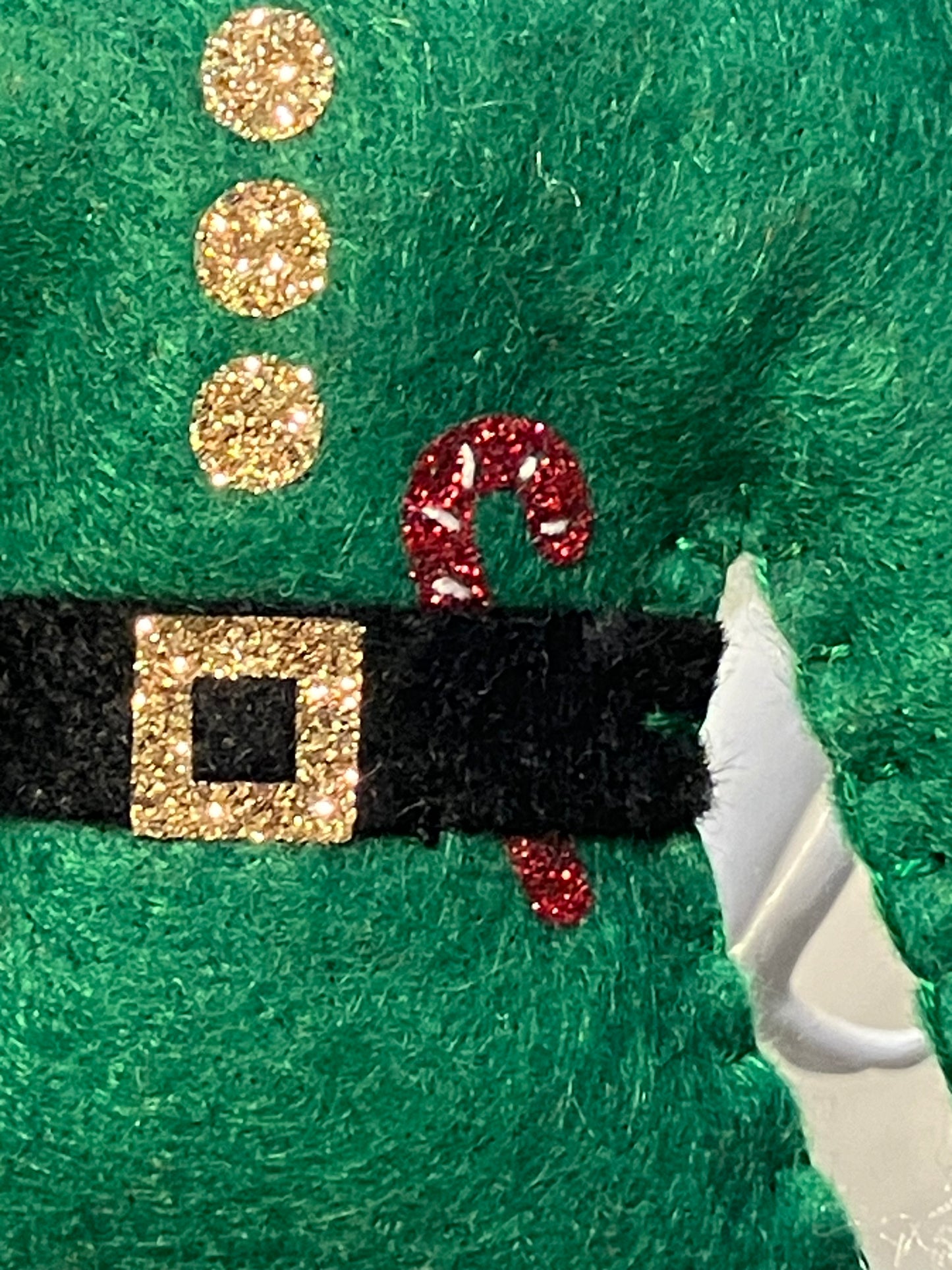 Close-up of green felt elf shirt with gold glitter buttons and red glitter candy cane.