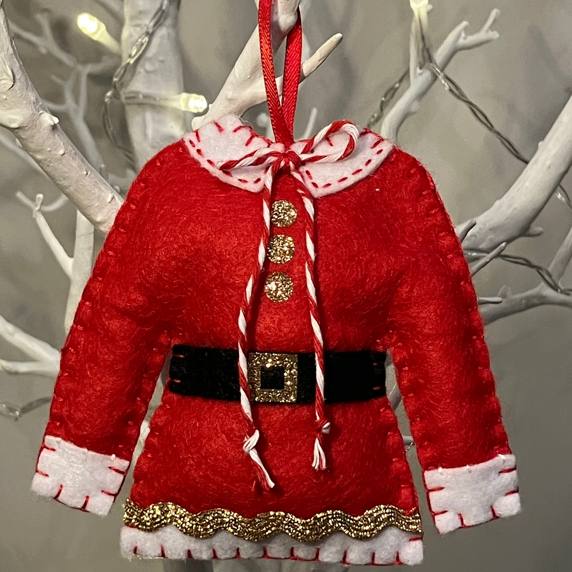 A close-up of a festive Santa's jacket hanging on a white branch for Christmas decoration.