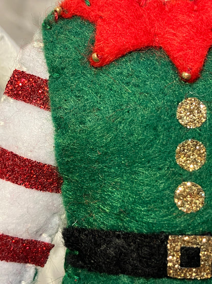 Close-up of the green felt elf costume ornament's side and striped sleeve.