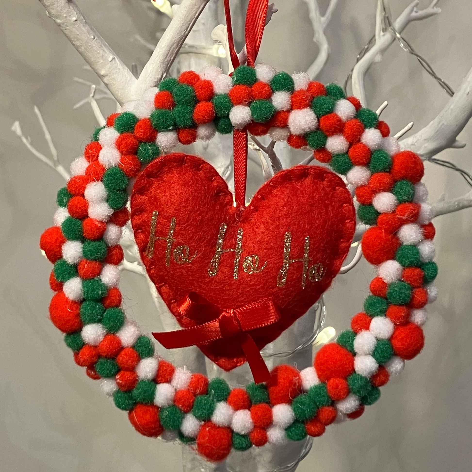 A red, white, and green pom-pom wreath with a red heart that says Ho Ho Ho.