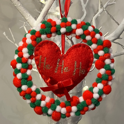 A red, white, and green pom-pom wreath with a red heart that says Ho Ho Ho.