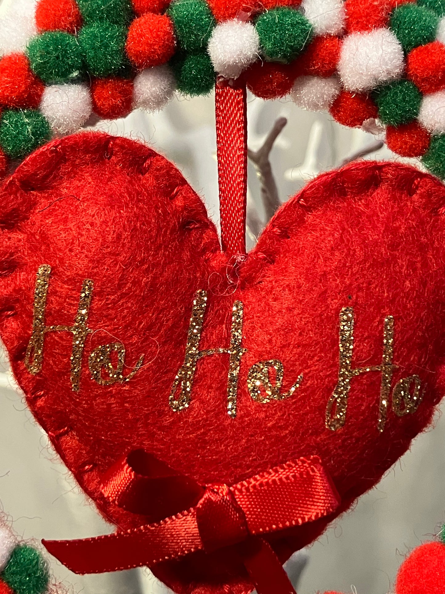 Close-up of a red felt heart ornament with Ho Ho Ho in gold glitter.