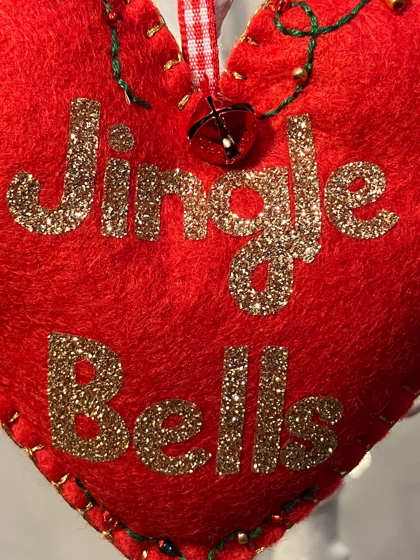 Close-up of the Jingle Bells text in gold glitter on a red felt heart ornament.
