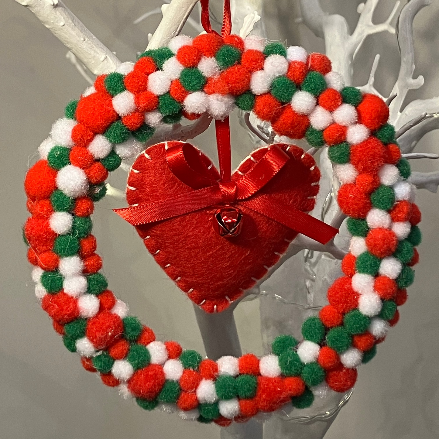 A red, white, and green pom-pom wreath with a red felt heart in the center.
