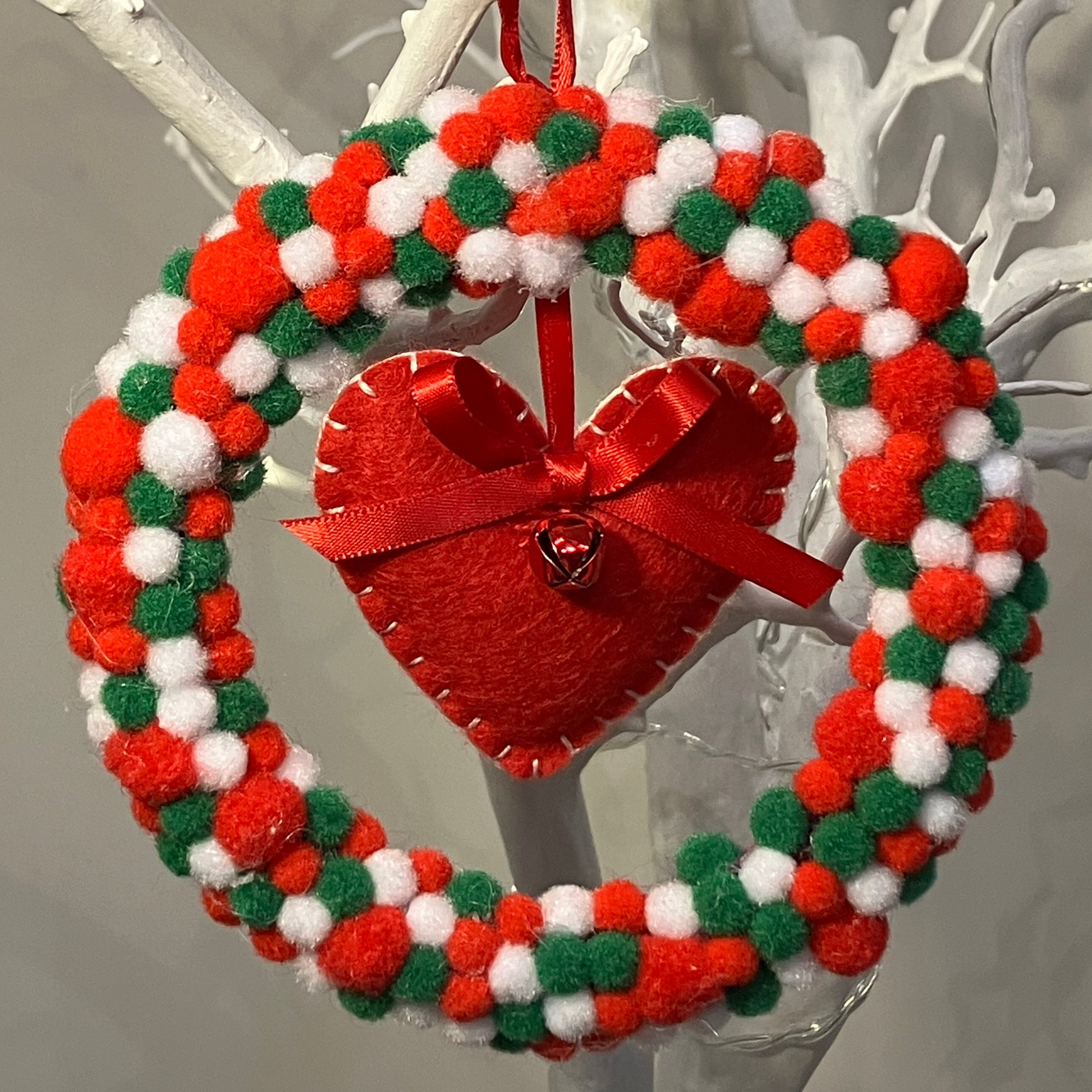 A red, white, and green pom-pom wreath with a red felt heart in the center.