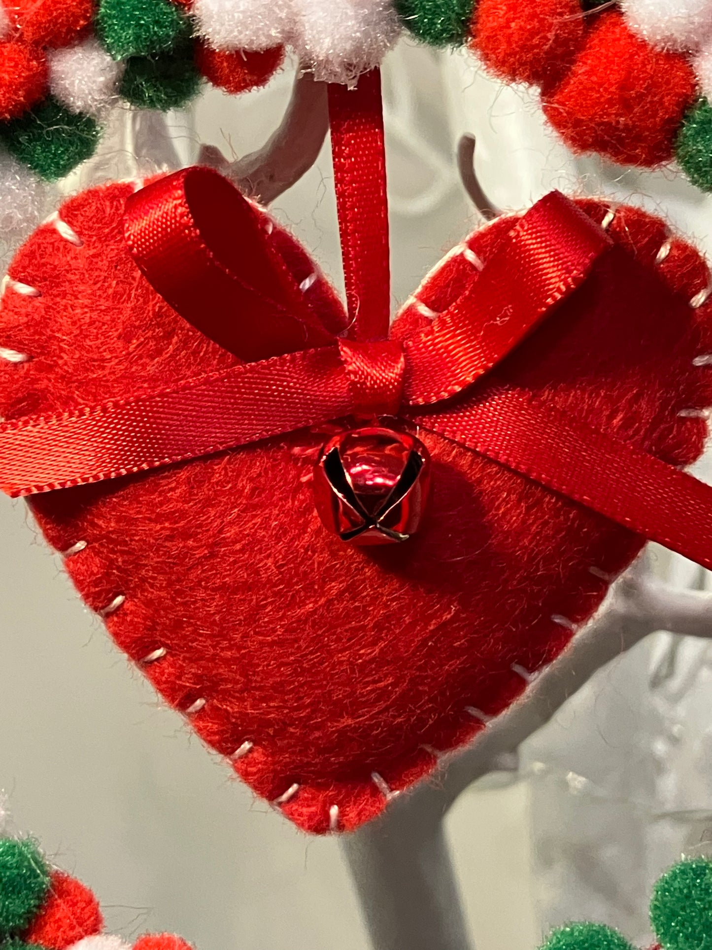 Close-up of a red felt heart ornament with a red ribbon and small bell.