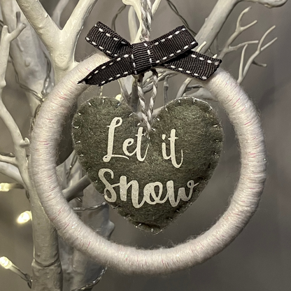 A white yarn wreath with a gray felt heart saying Let it Snow.