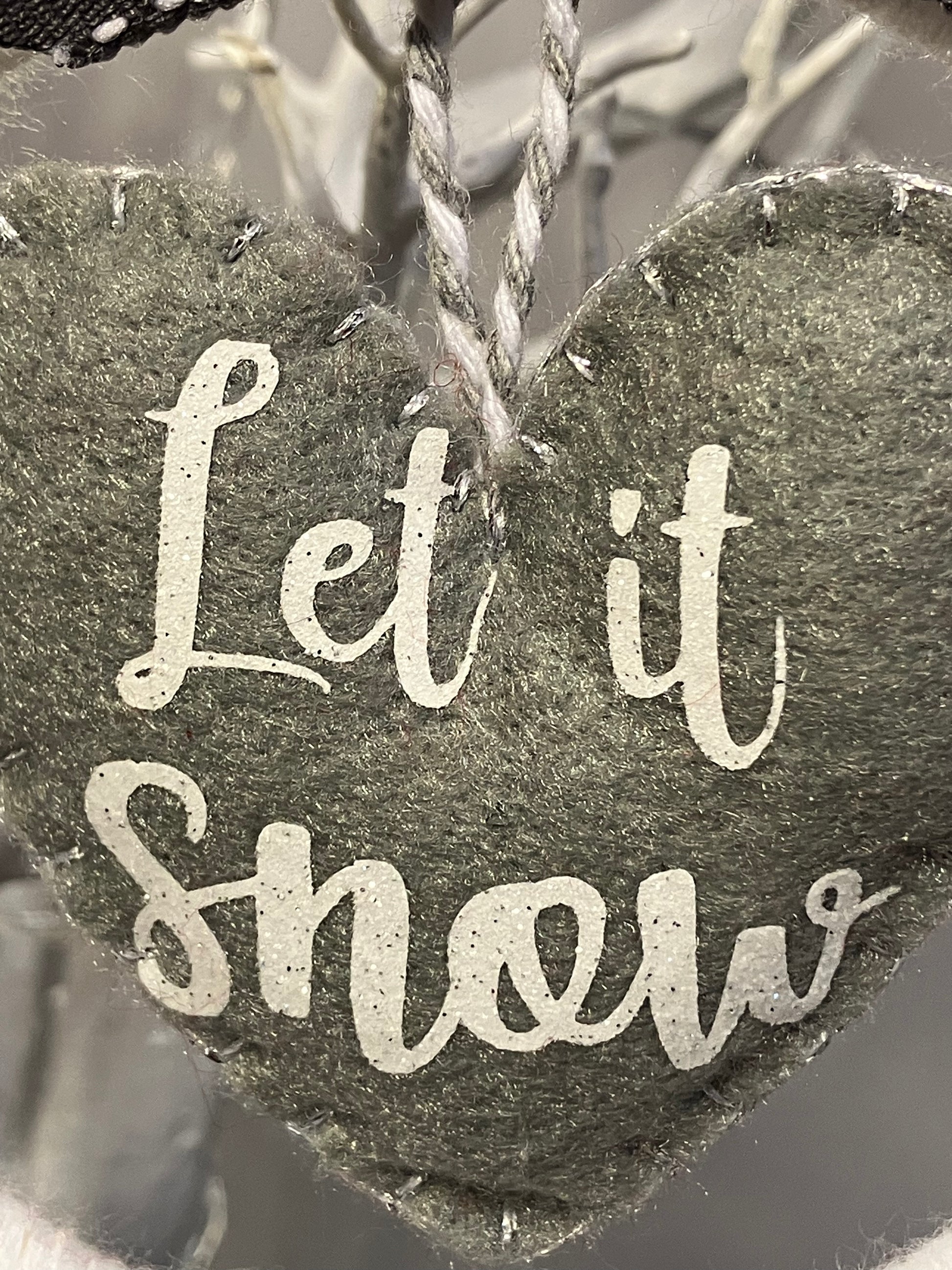 Close-up of the white Let it Snow text on a gray felt heart ornament.