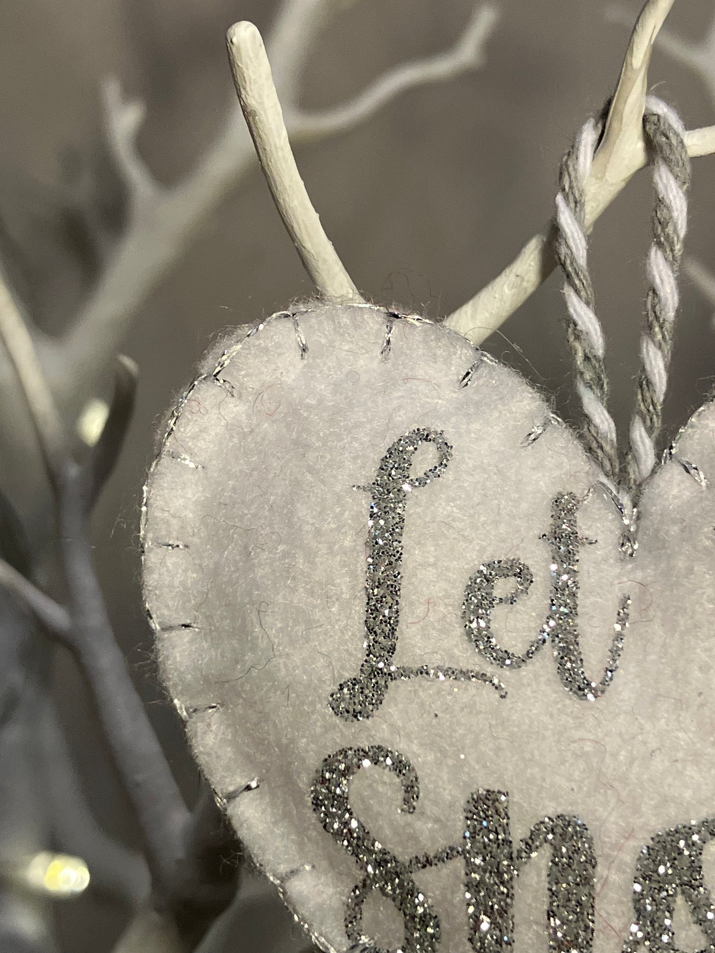 Close-up of the silver glitter Let it Snow text on a white felt heart ornament.