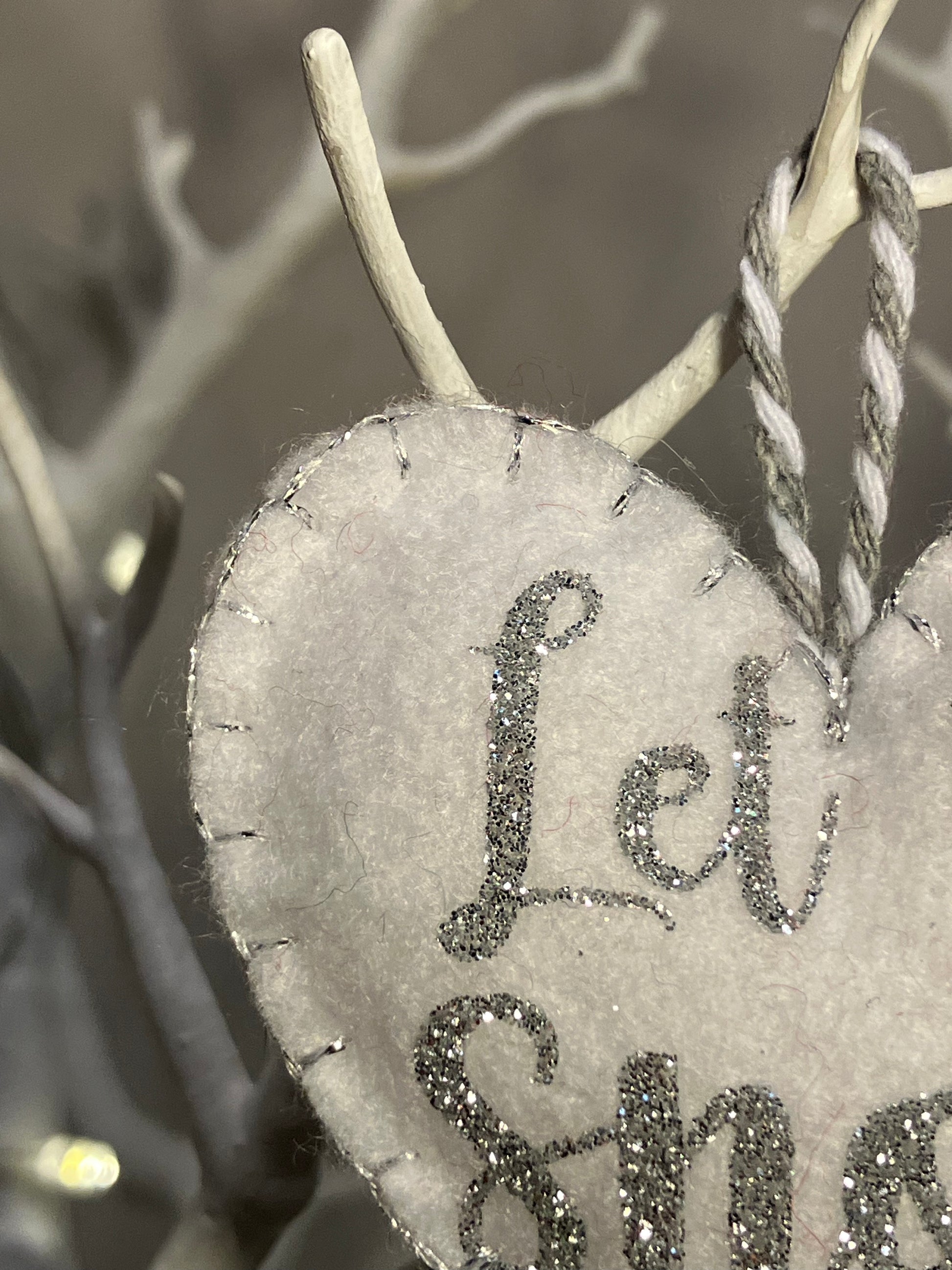 Close-up of the silver glitter Let it Snow text on a white felt heart ornament.