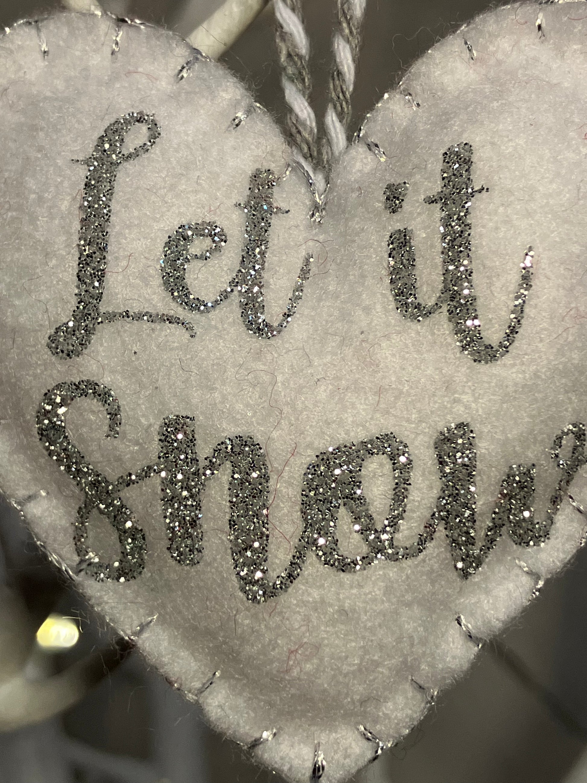 Close-up of the silver glitter Let it Snow text on a white felt heart ornament.