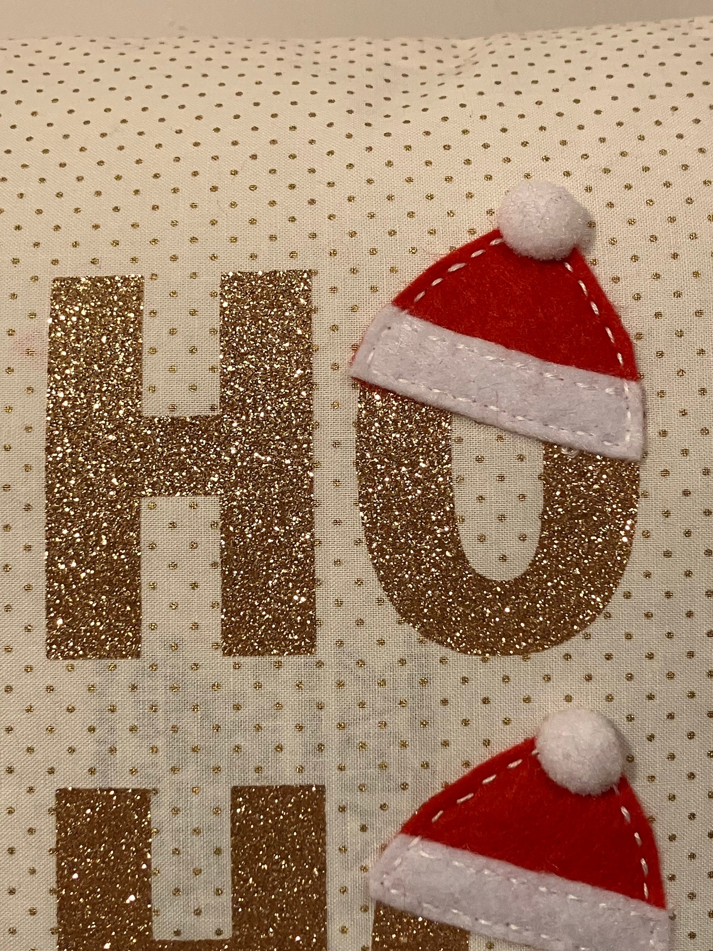 Close-up of the glittery gold HO with a Santa hat on the O on a dotted pillow.