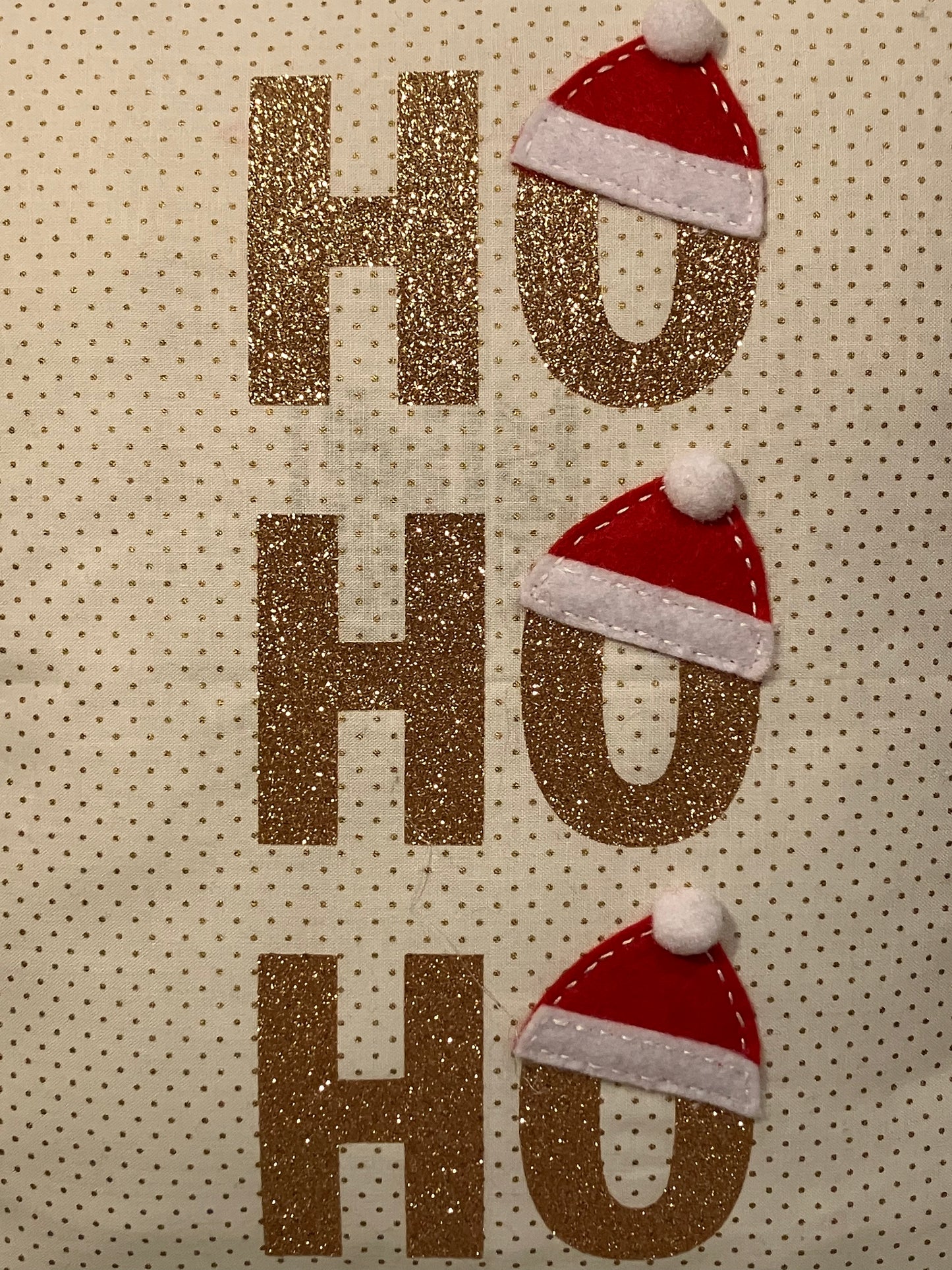 Detailed view of the three HO HO HO phrases in glittery gold with Santa hats.