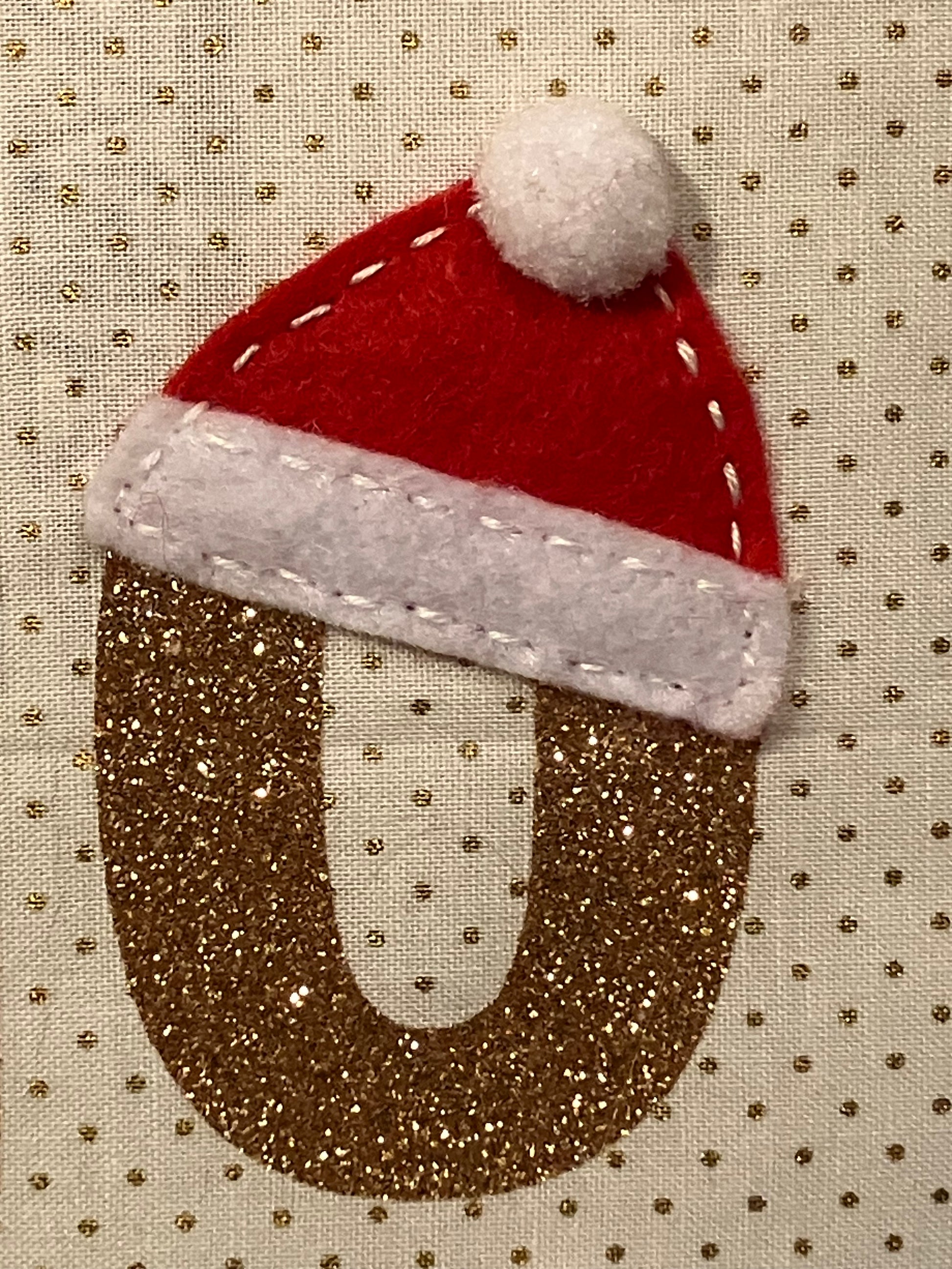 A close-up of a glittery gold 'O' with a small Santa hat on top.