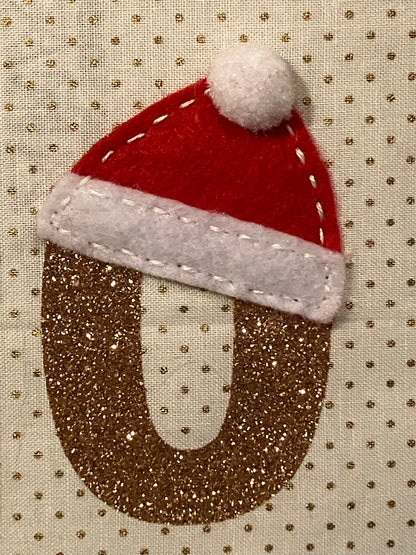 A close-up of a glittery gold 'O' with a small Santa hat on top.