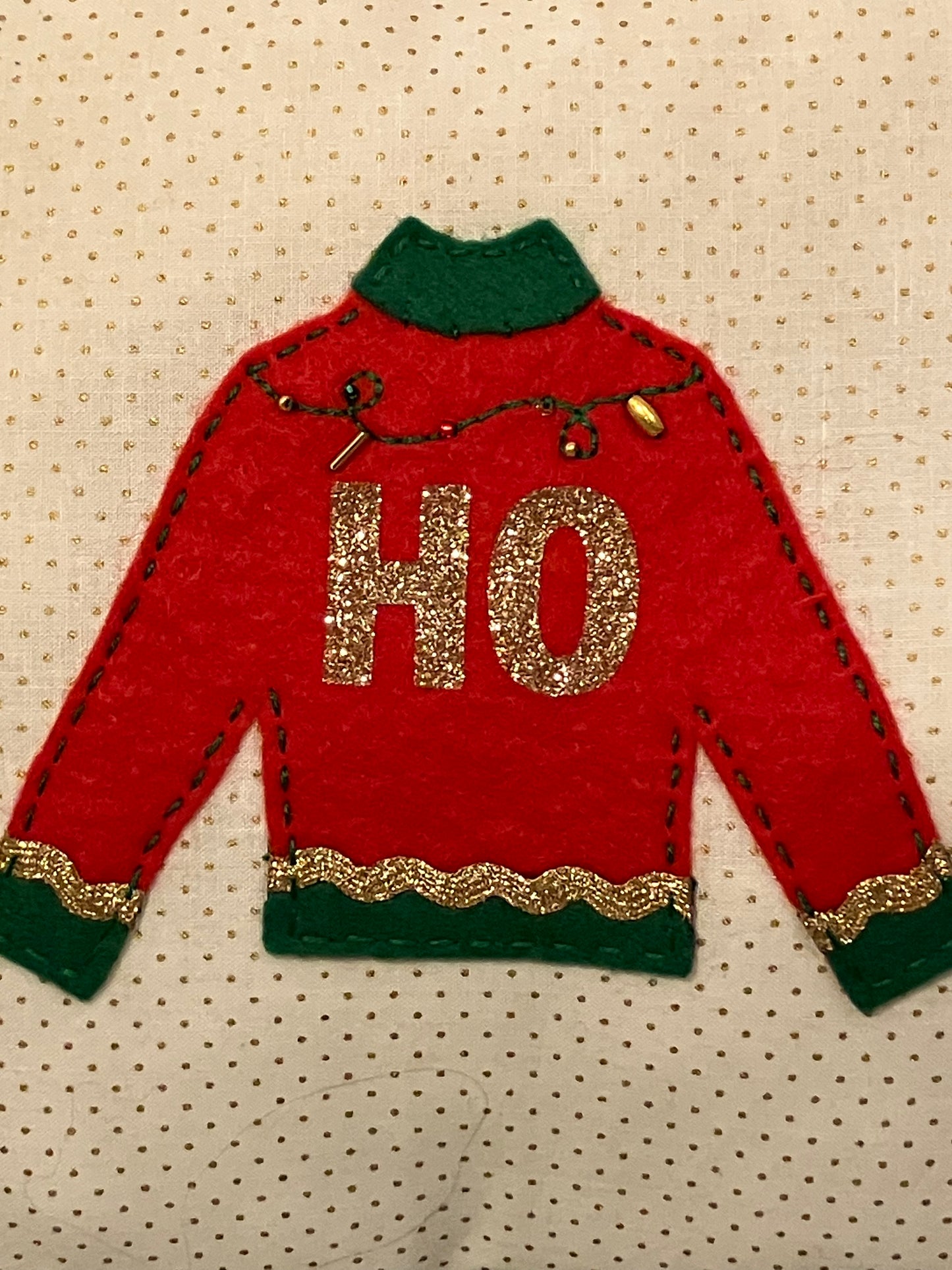 A close-up of a red and green sweater with "HO" in gold glitter.