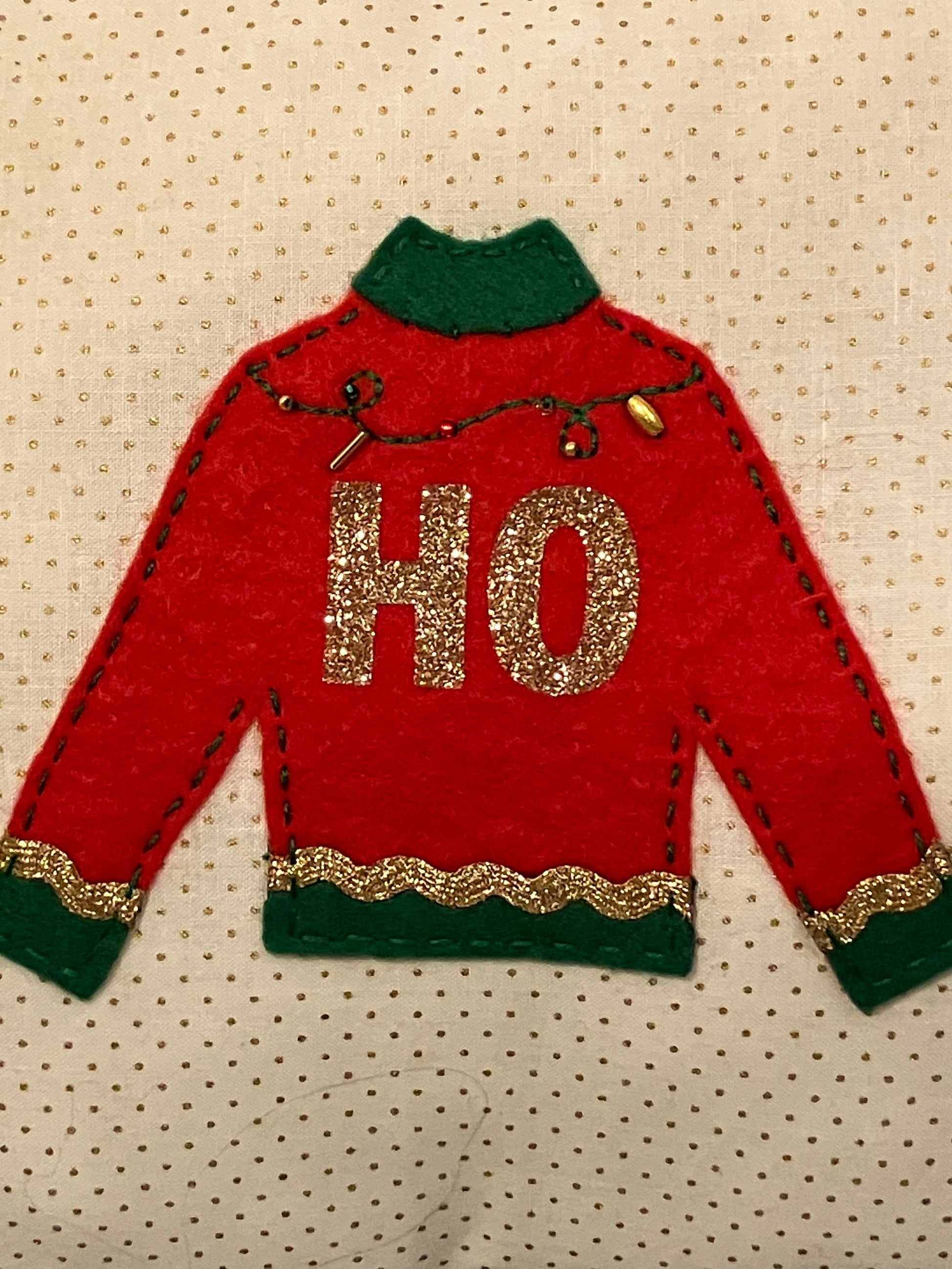 A close-up of a red and green sweater with "HO" in gold glitter.