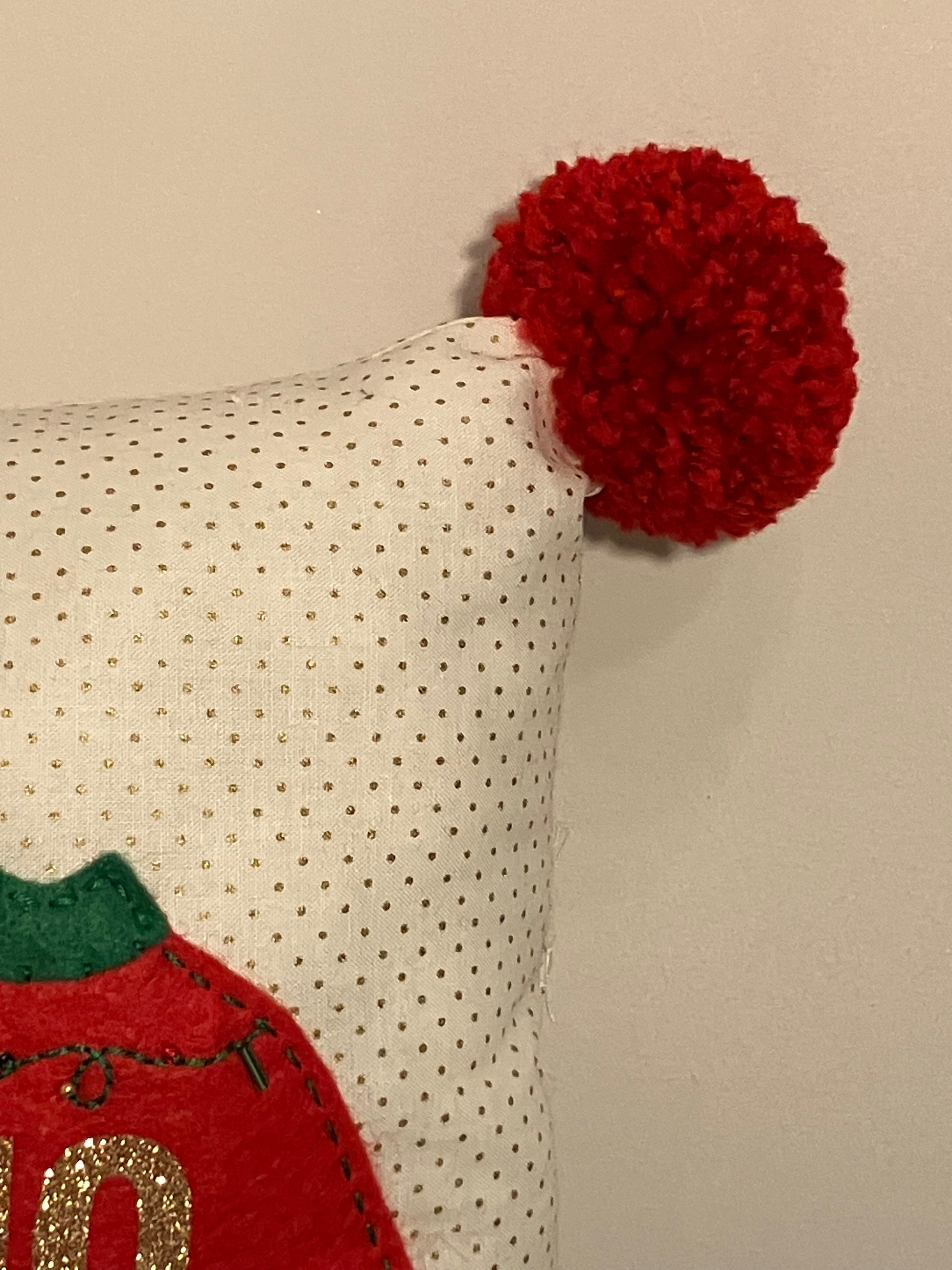 A corner of the pillow, showing a red pom-pom and dotted white fabric.