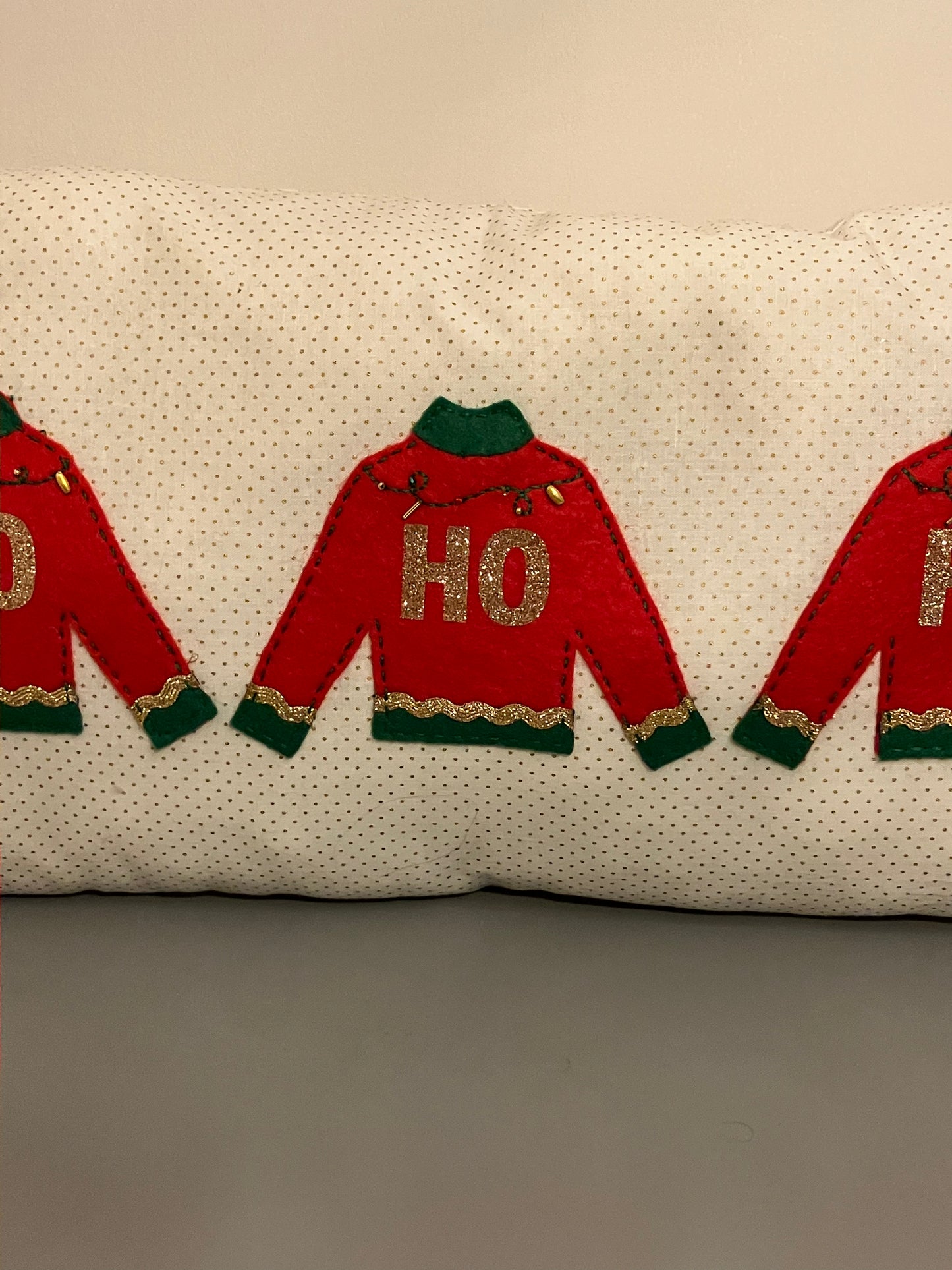 A close-up of the pillow showing the three red sweaters with "HO" in gold glitter.