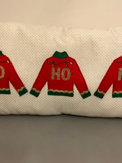 A close-up of the pillow showing the three red sweaters with "HO" in gold glitter.