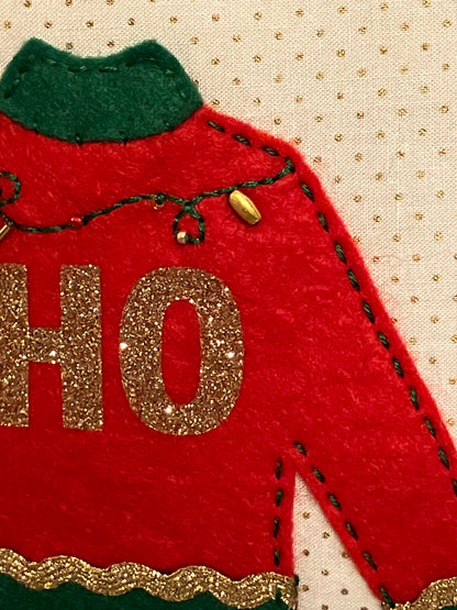 A detailed view of one red sweater on the pillow with gold glitter "HO".