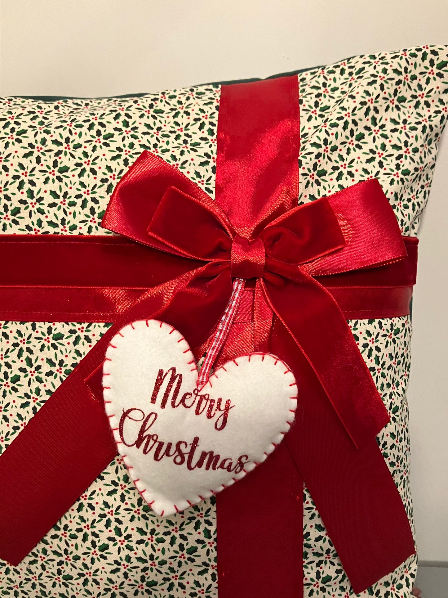 Close-up of a festive cushion with holly pattern, red ribbon, and 'Merry Christmas' tag.