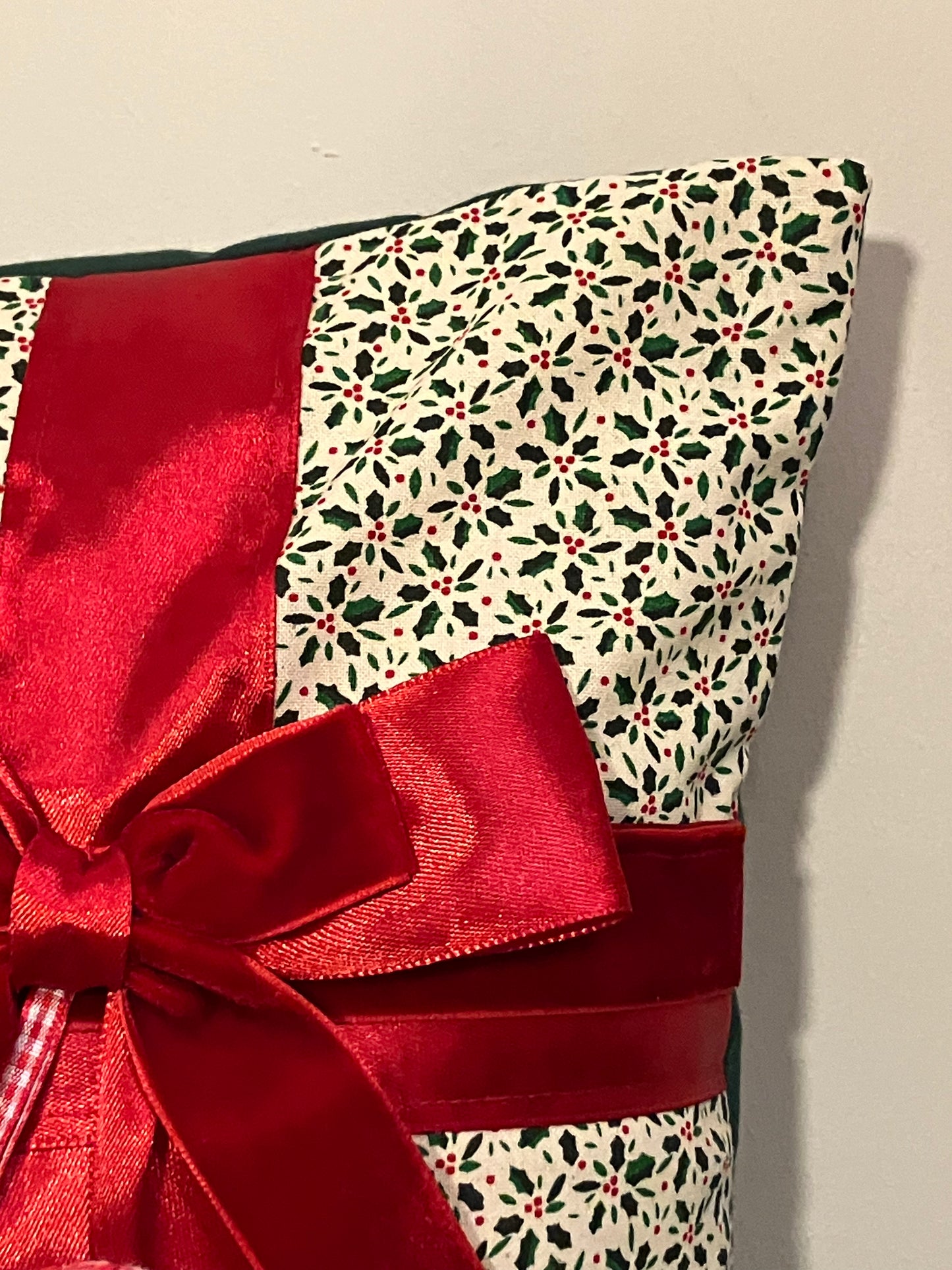 A corner of the holly-patterned cushion, featuring a red ribbon and bow detail.