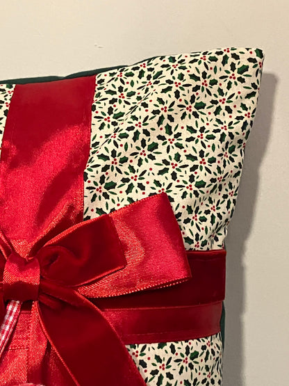 A corner of the holly-patterned cushion, featuring a red ribbon and bow detail.