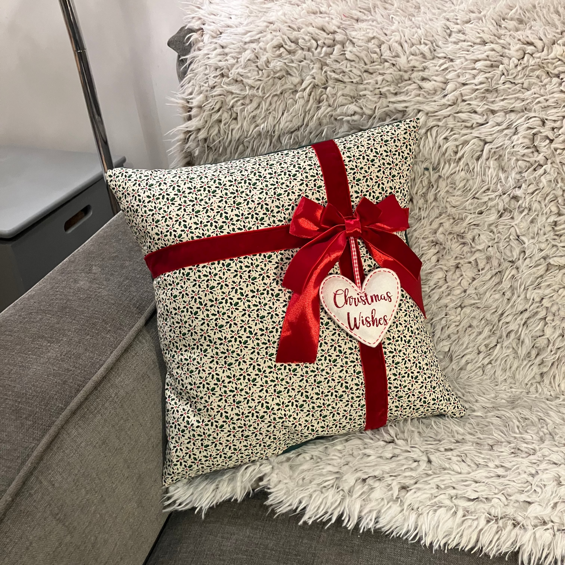Christmas cushion with red ribbon and 'Christmas Wishes' heart, resting on a fluffy blanket.