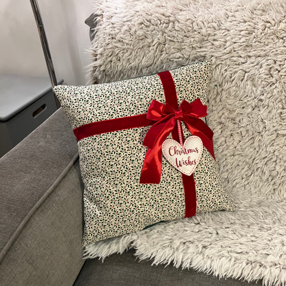 Christmas cushion with red ribbon and 'Christmas Wishes' heart, resting on a fluffy blanket.