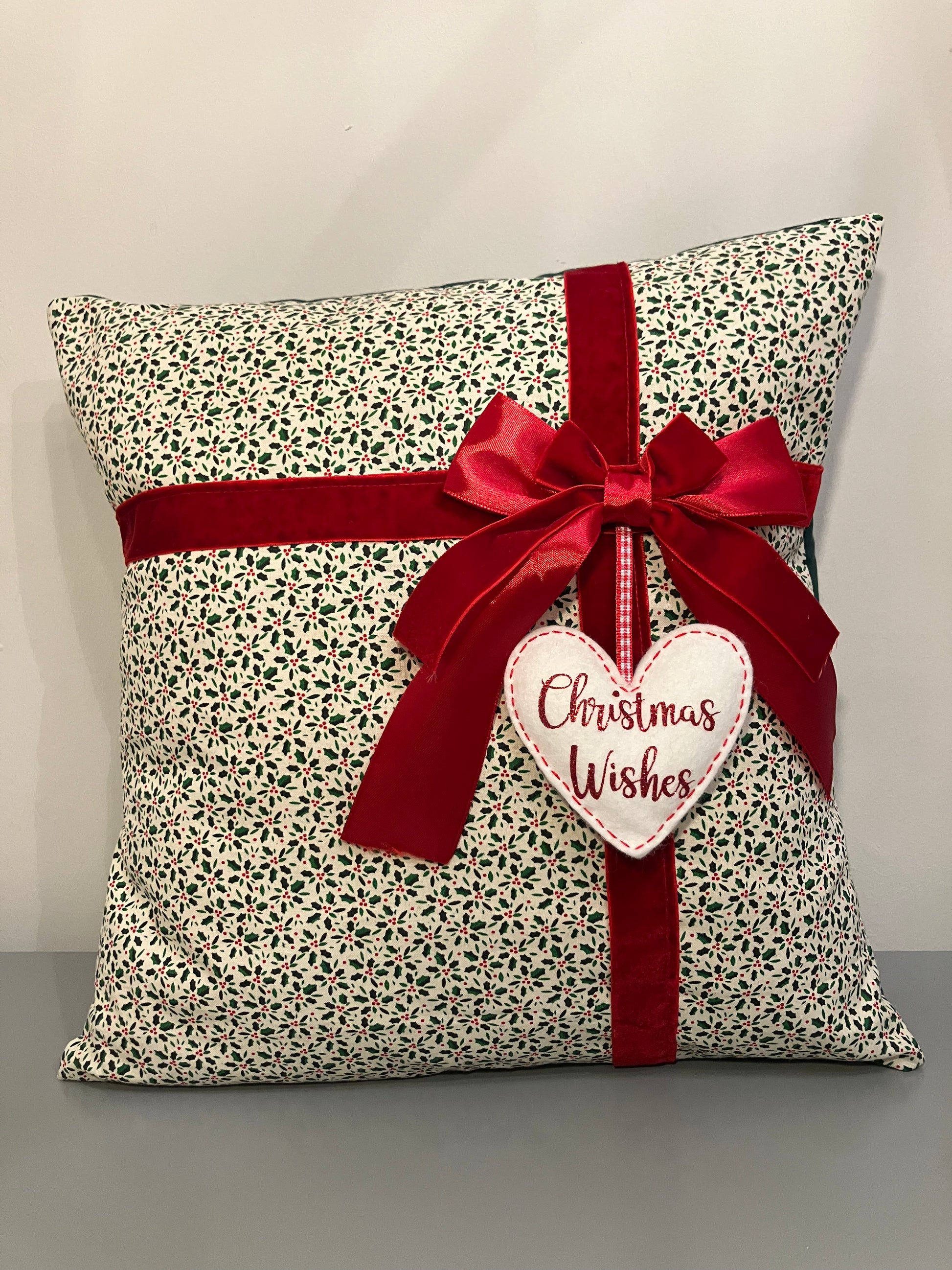 Christmas cushion with a festive pattern, red ribbon, and a 'Christmas Wishes' heart.