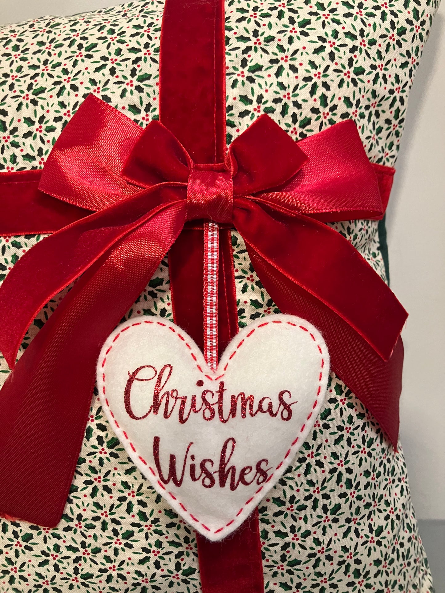 Close-up of a Christmas cushion featuring a red bow and a 'Christmas Wishes' heart.