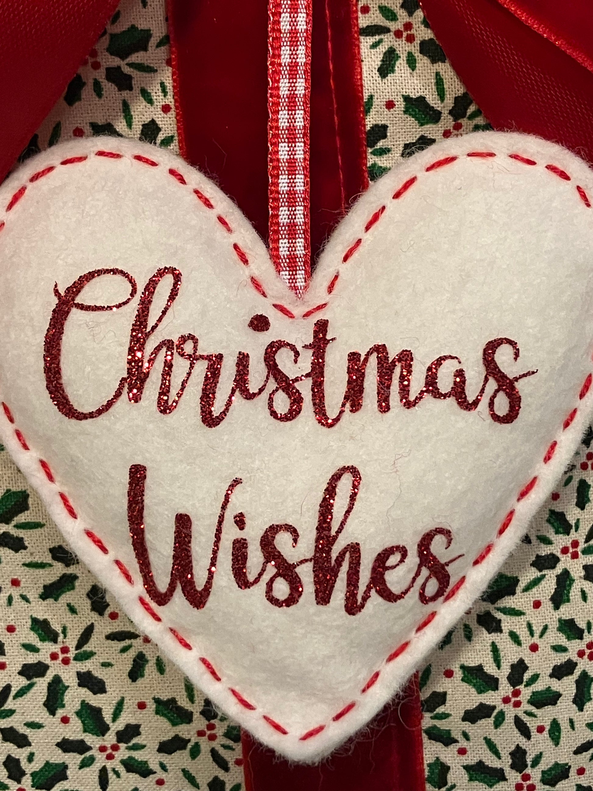 Close-up of a white heart decoration with 'Christmas Wishes' in red glitter text.