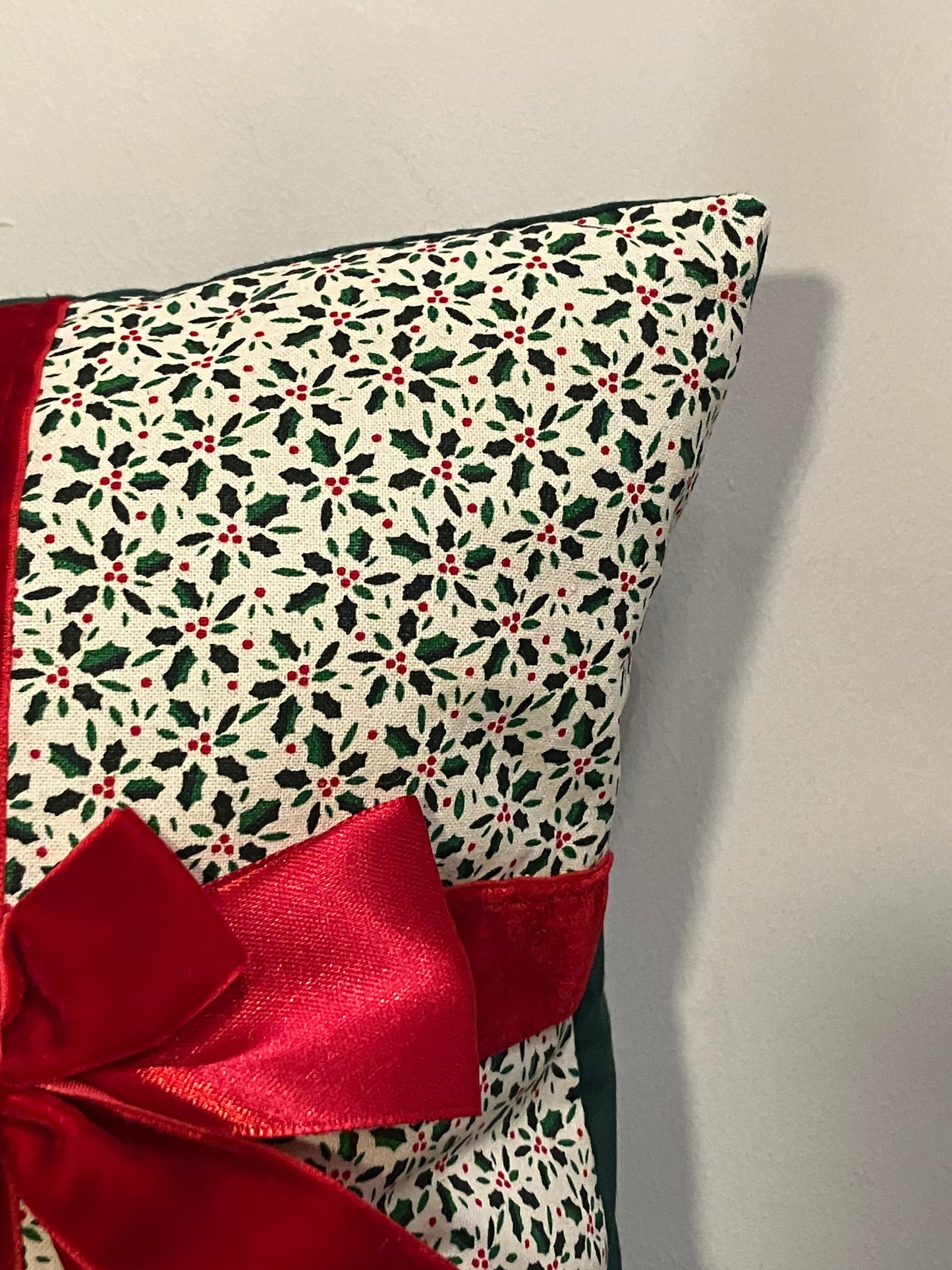 Corner of a festive Christmas cushion with a holly pattern and a red satin bow.