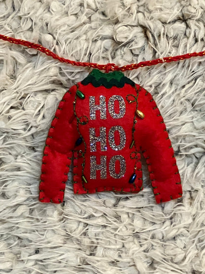 A felt red sweater ornament with "HO HO HO" and tiny Christmas lights on a white surface.