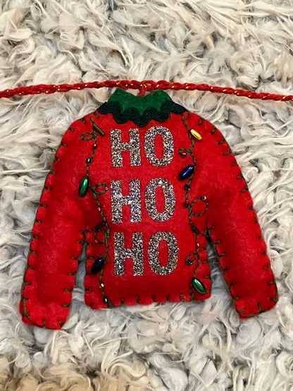 A felt red sweater ornament with "HO HO HO" and tiny Christmas lights on a white surface.