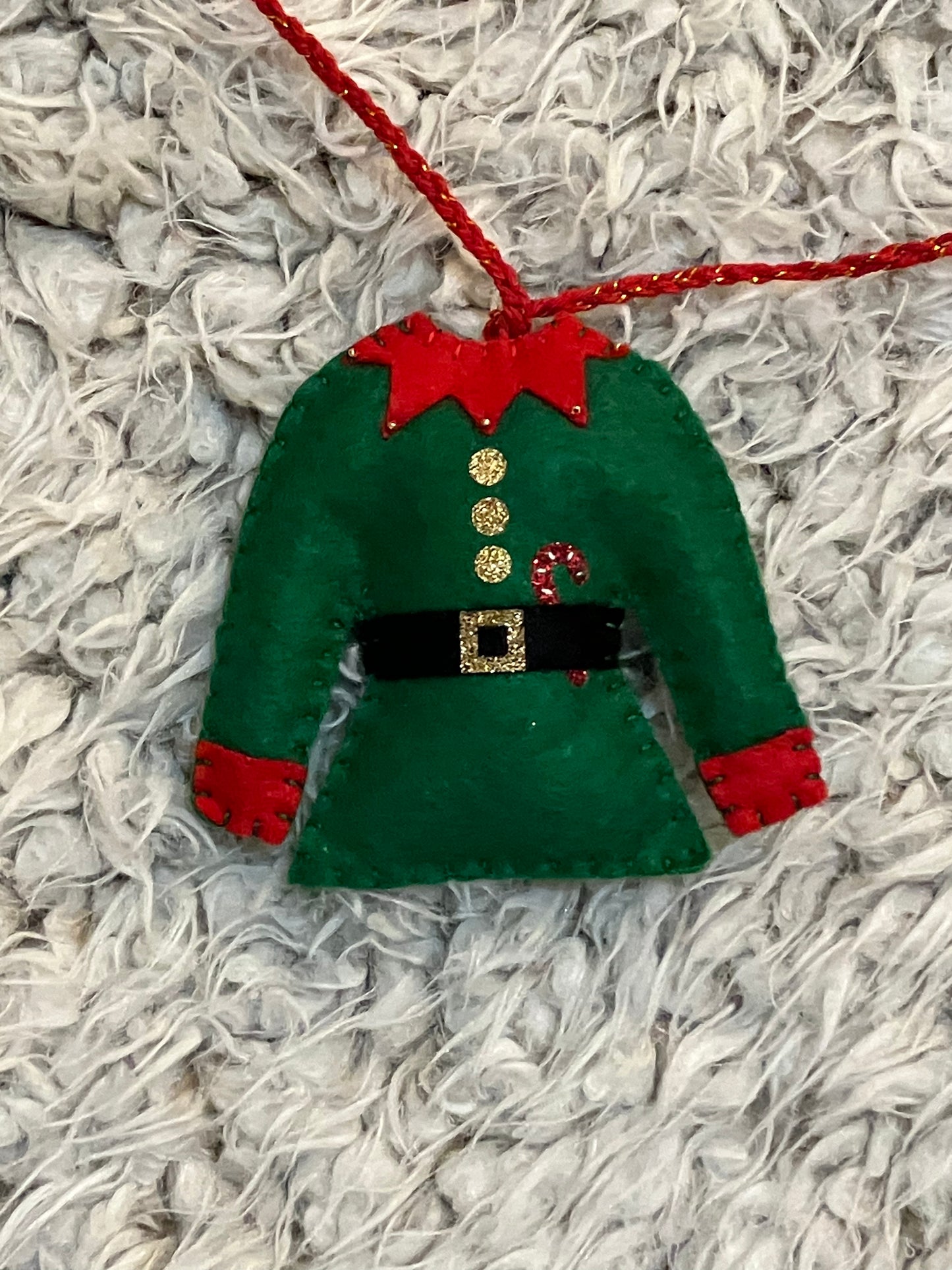 A closeup of a single green elf outfit with red trim, gold buttons, and a candy cane.