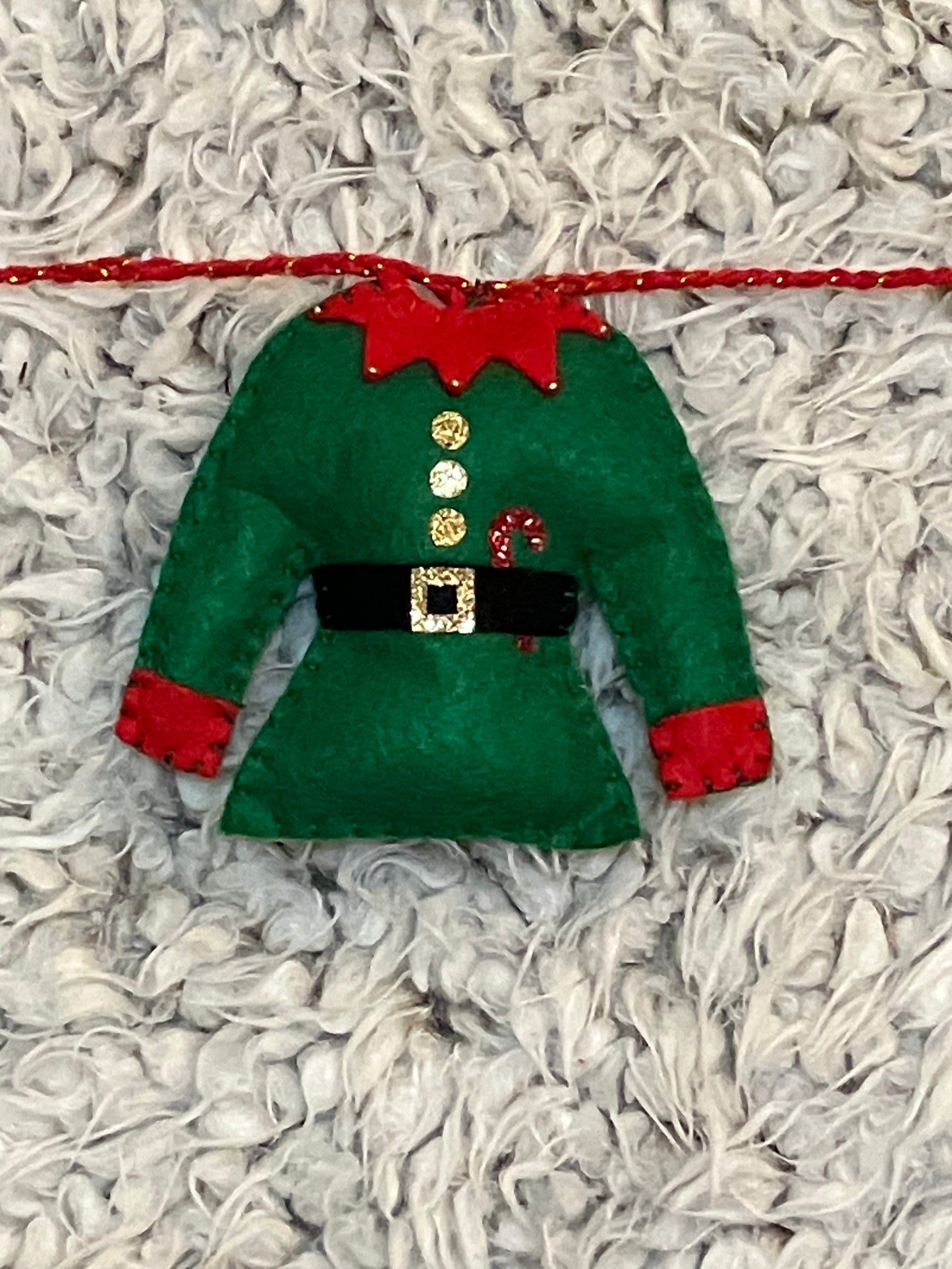 A closeup of a single green elf outfit with red trim, gold buttons, and a candy cane.
