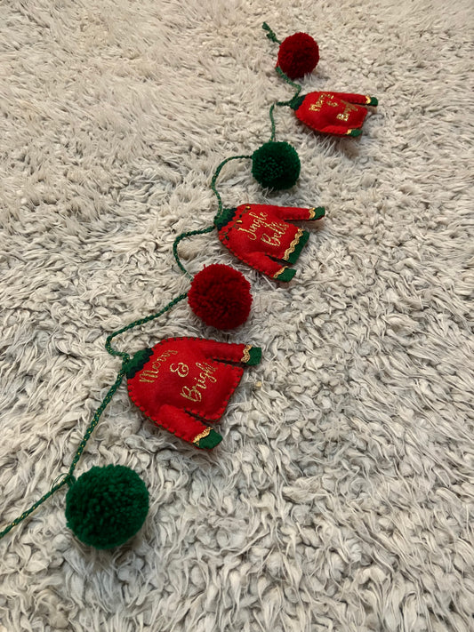 Christmas sweater garland featuring red sweaters and green and red pom poms on a gray rug.