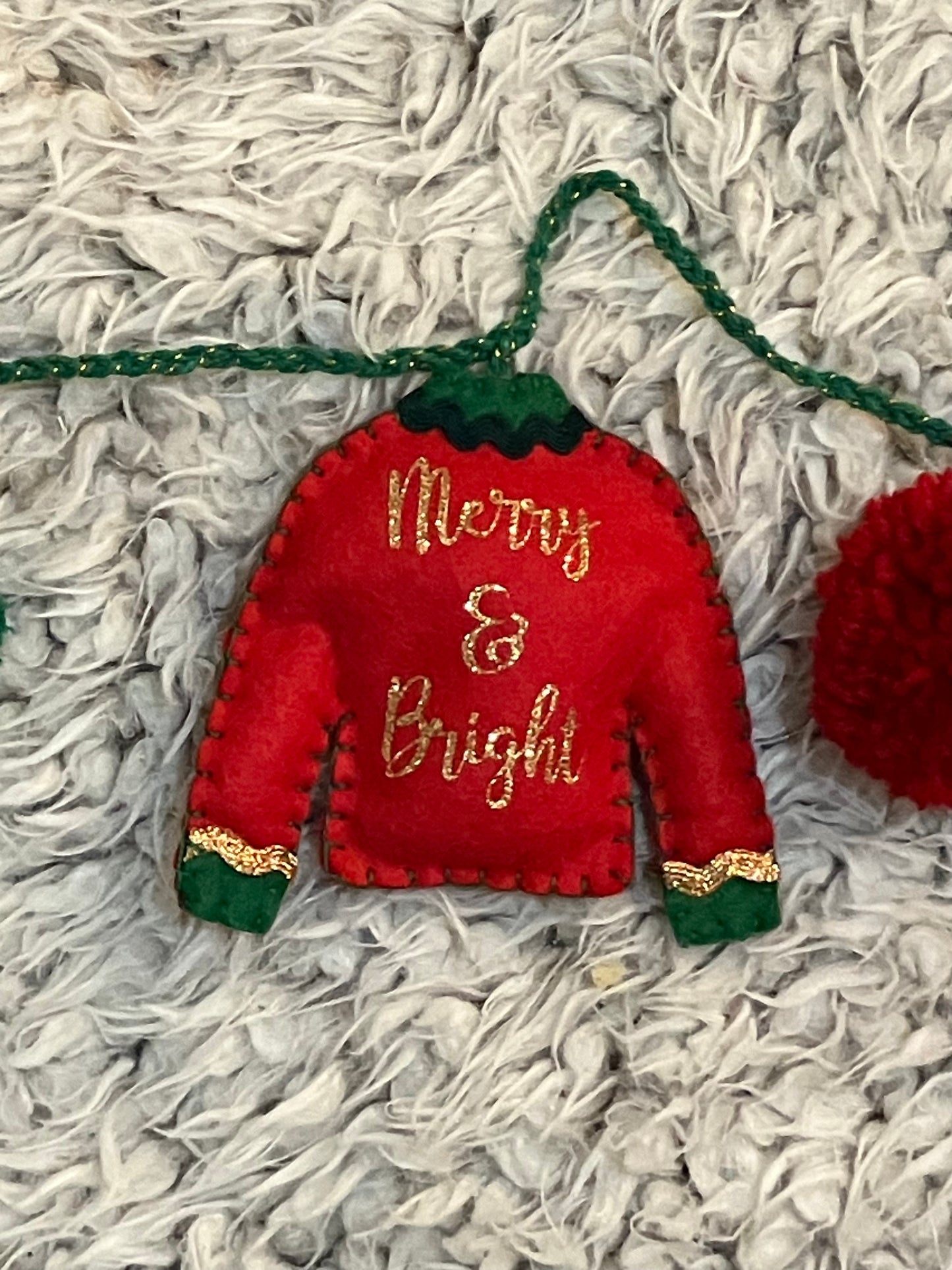 Close-up of red felt Christmas sweater ornament with "Merry & Bright" in gold glitter.
