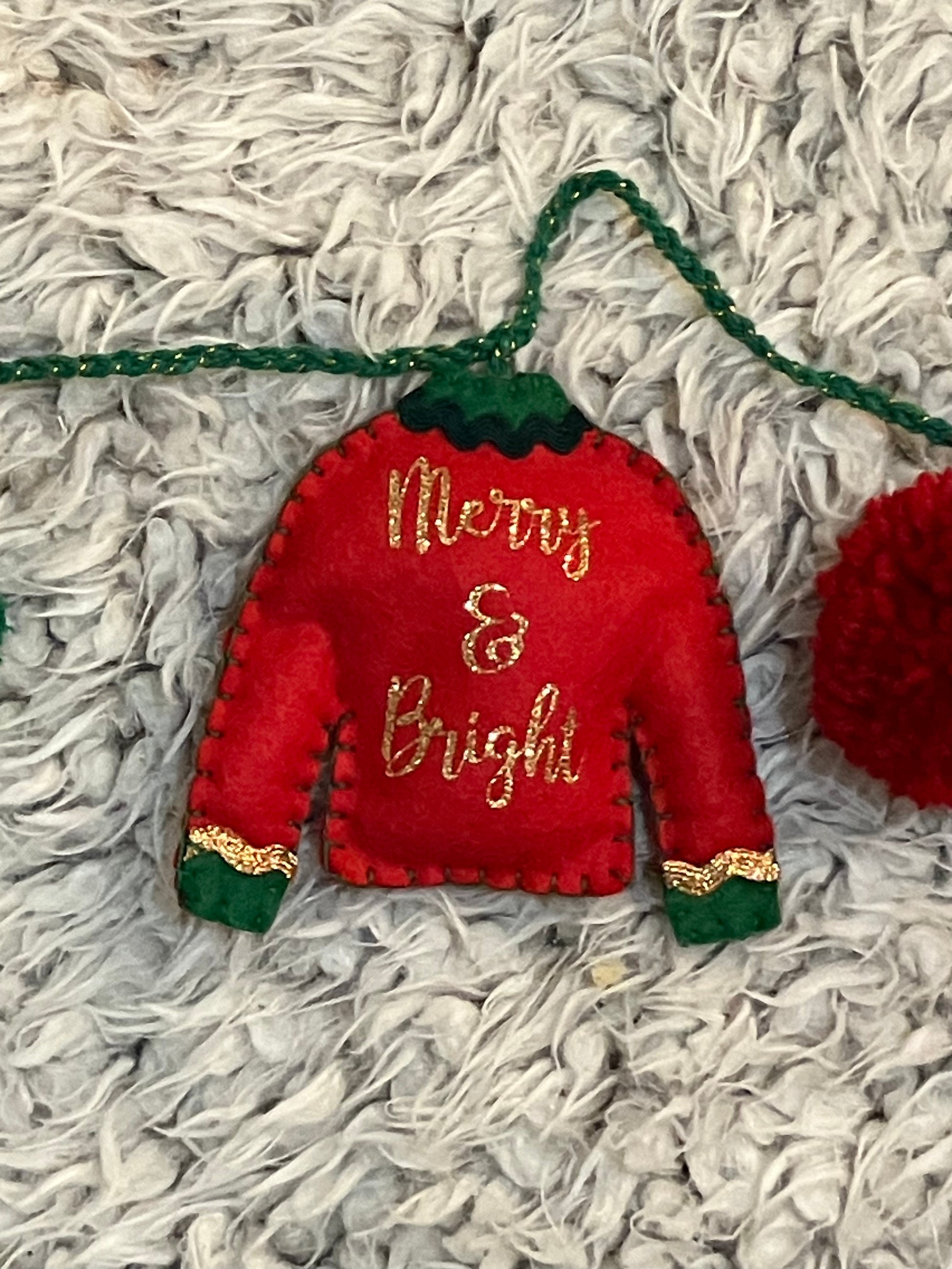 Close-up of red felt Christmas sweater ornament with "Merry & Bright" in gold glitter.
