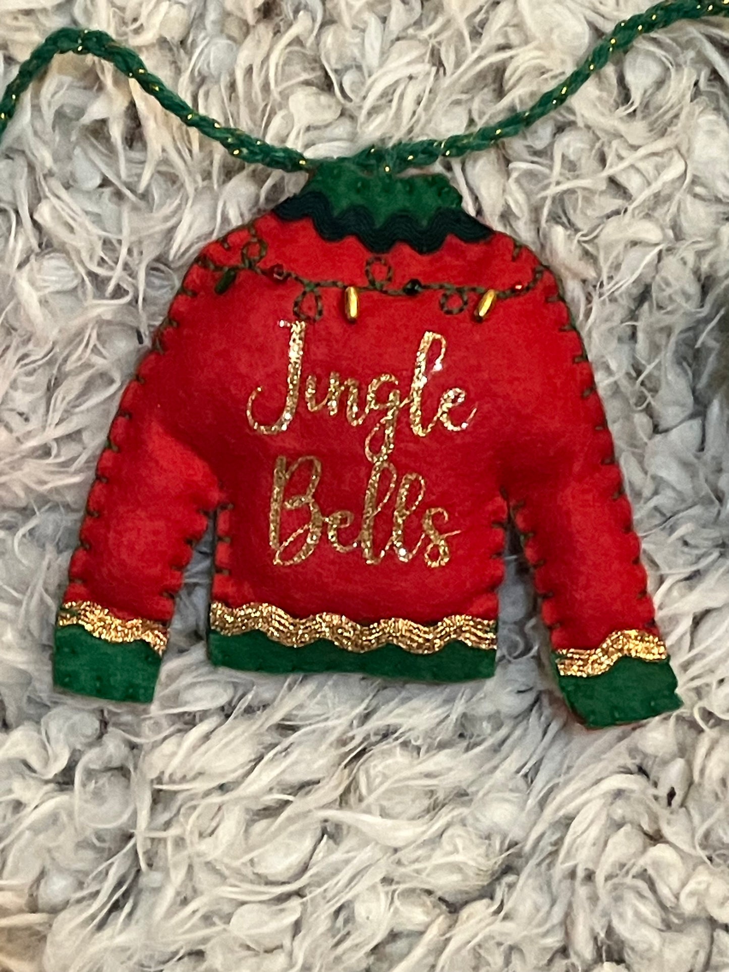 Close-up of red felt Christmas sweater ornament with "Jingle Bells" in gold glitter.