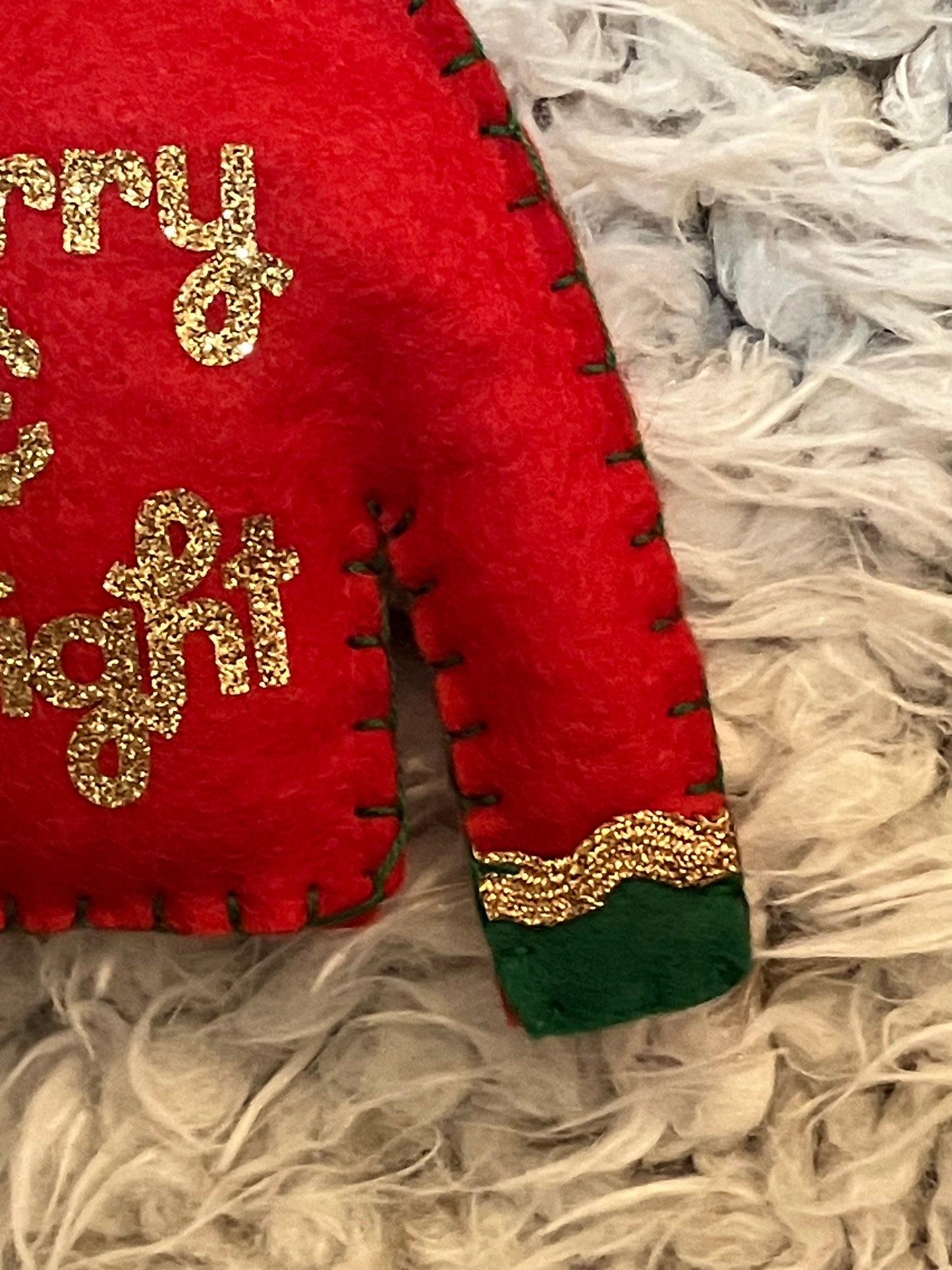 Detail of red felt Christmas sweater ornament sleeve with green cuff and gold glitter trim.